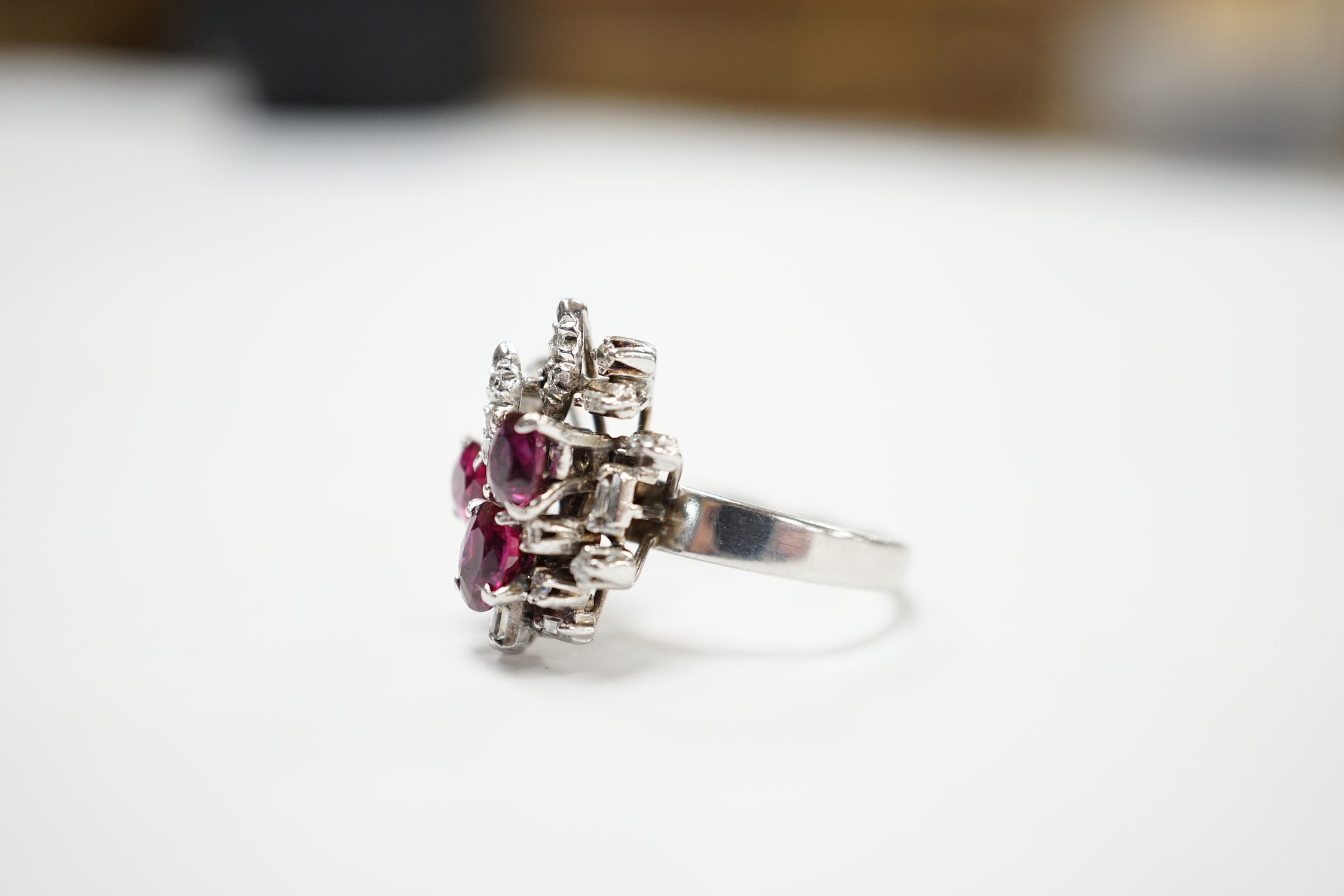 A recent 18k white metal, ruby and diamond cluster set modernist dress ring, size N/O, gross weight 5.7 grams.